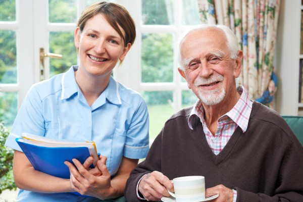 Nurse smiling alongside an older man enjoying a cup of tea